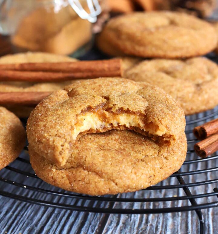 chewy pumpkin cheesecake cookies stacked on cooling rack with bite showing creamy cheesecake filling