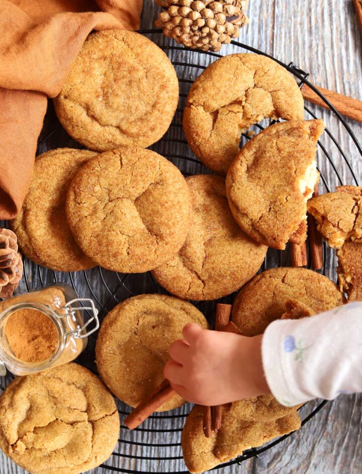 top view of pumpkin cheesecake cookies piled up on cooling rack with bite showing cheesecake filling