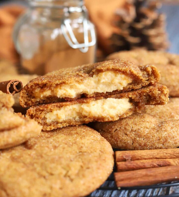 pumpkin cheesecake cookies piled up on cooling rack with cookie split in half showing creamy cheesecake filling