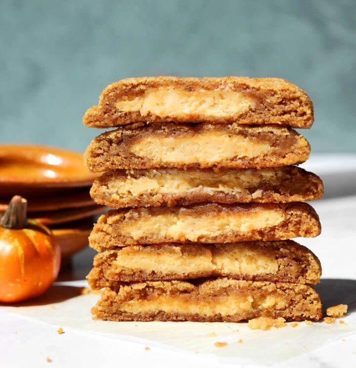 stack of pumpkin cheesecake cookies cut in half and showing creamy cheesecake filling