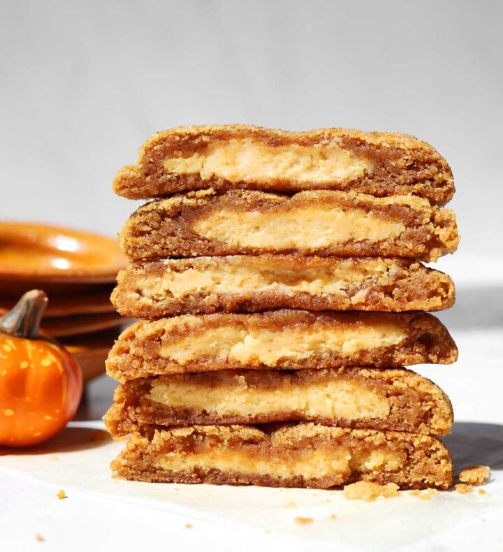 stack of pumpkin cheesecake cookies cut in half and showing creamy cheesecake filling