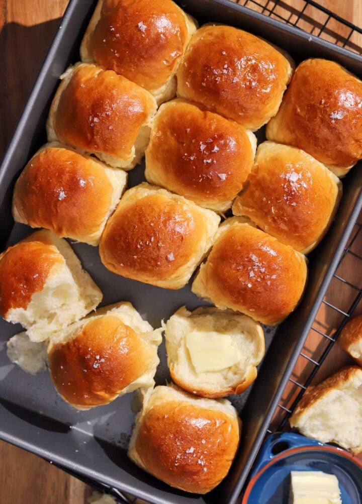 soft homemade dinner rolls in baking pan with some torn open rolls