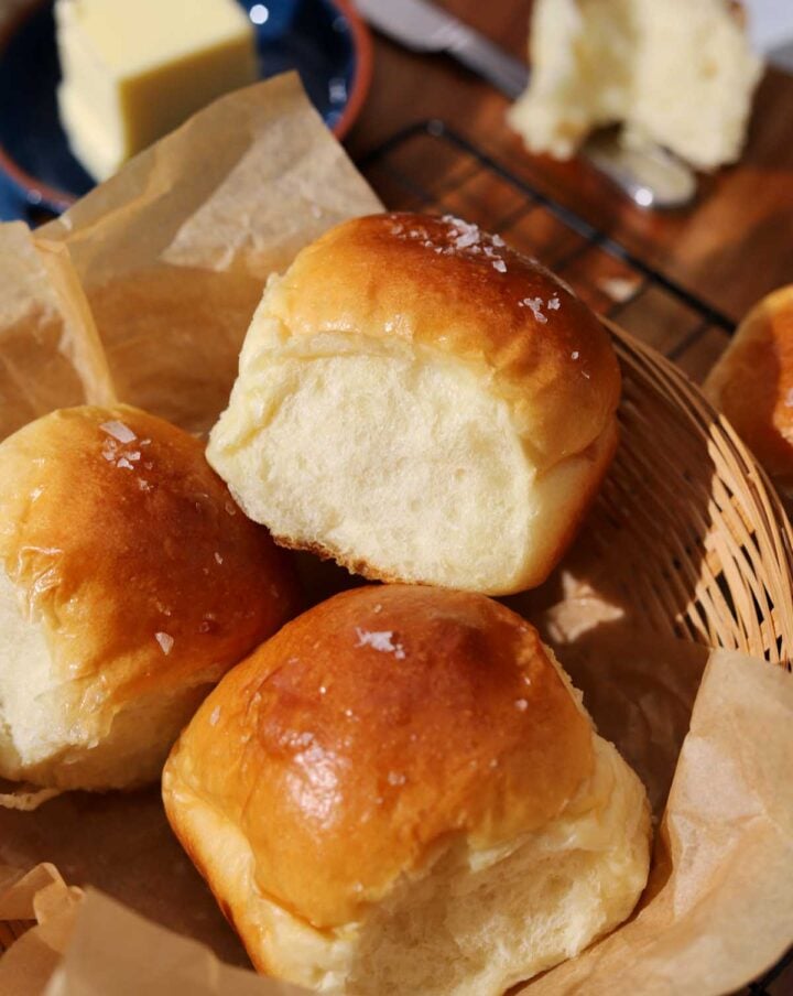 homemade dinner rolls in a basket with parchment paper