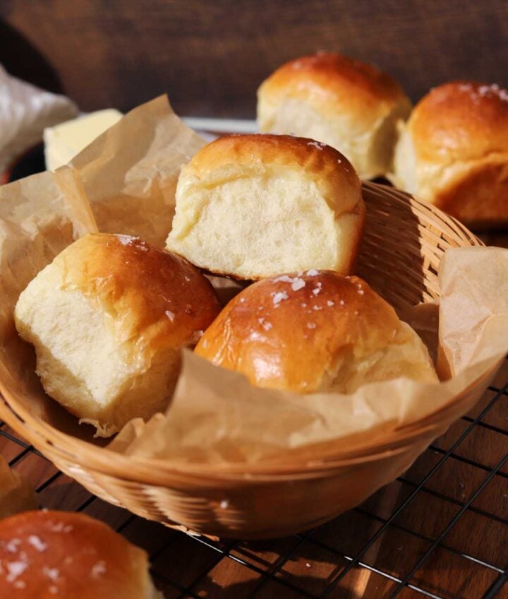 homemade dinner rolls in a basket with parchment paper