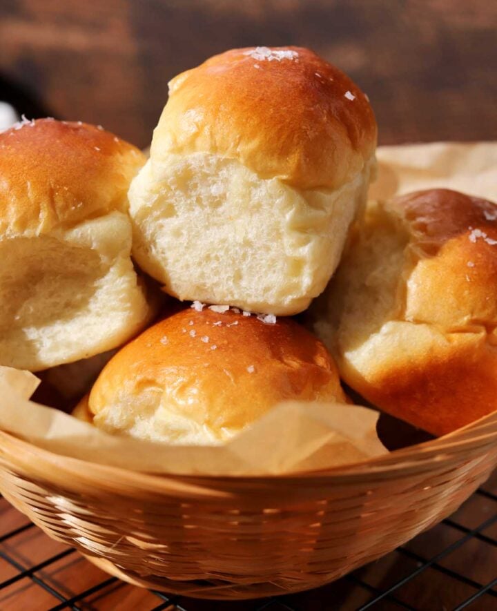 homemade dinner rolls in a basket with parchment paper