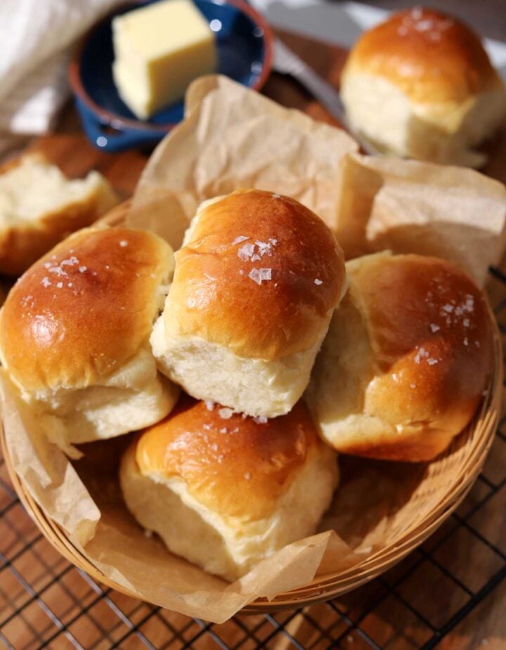 homemade dinner rolls in a basket with parchment paper