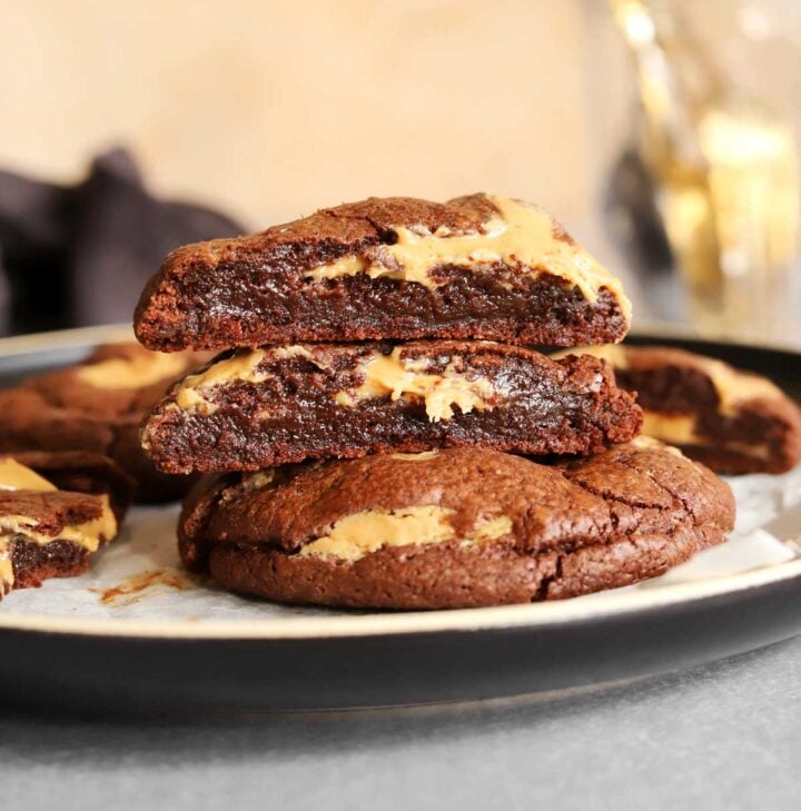 stack of peanut butter fudge swirl cookies broken in half on a plate showing fudgy texture