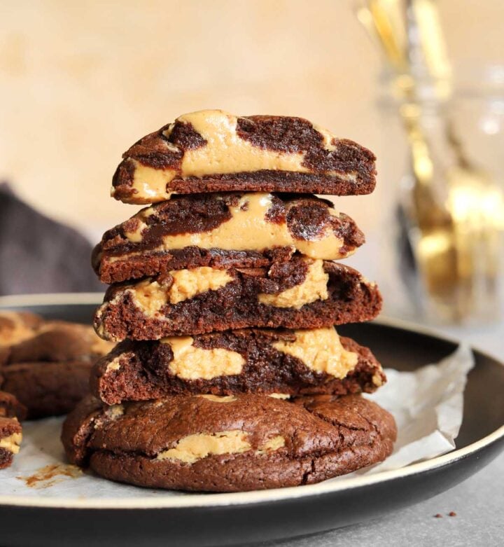 stack of chocolate peanut butter fudge swirl cookies broken in half on a plate showing fudgy texture