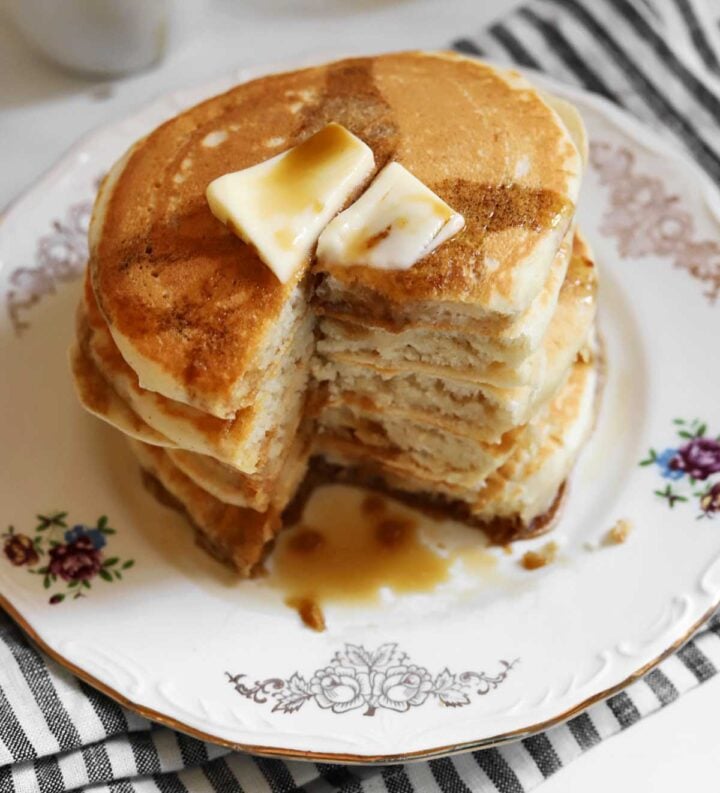 stack of fluffy egg white pancakes on a plate with bite and butter and maple syrup on top